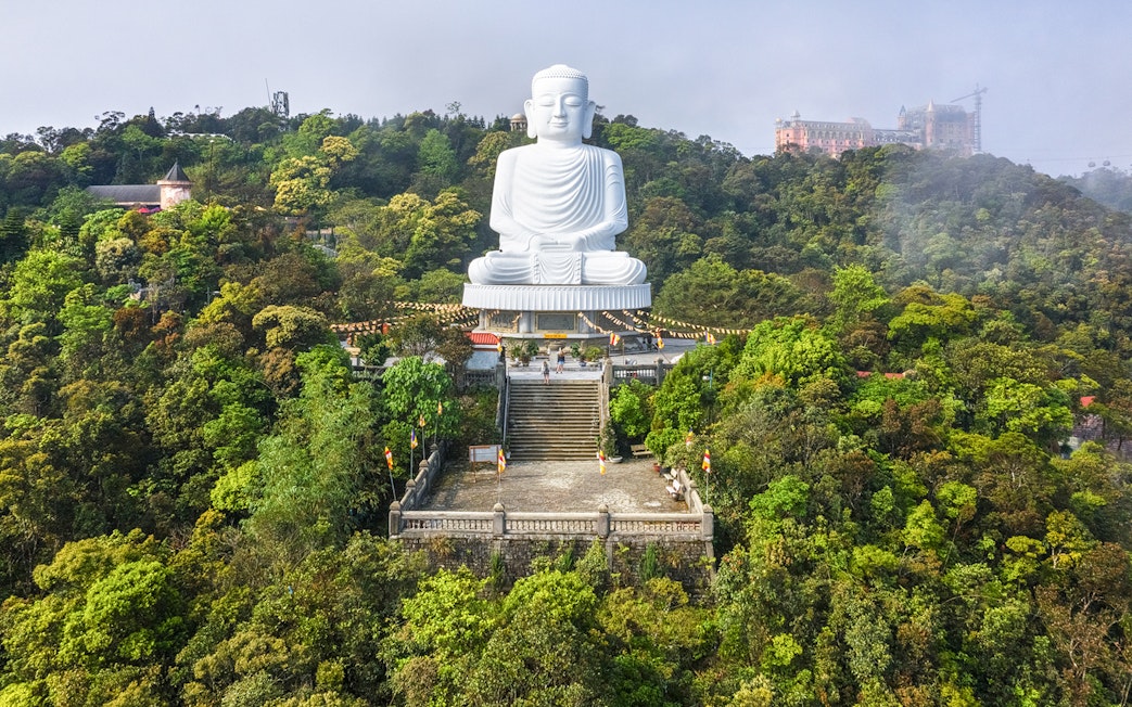 Buddha statue on Ba Na Hills, Vietnam, surrounded by lush greenery and mist.