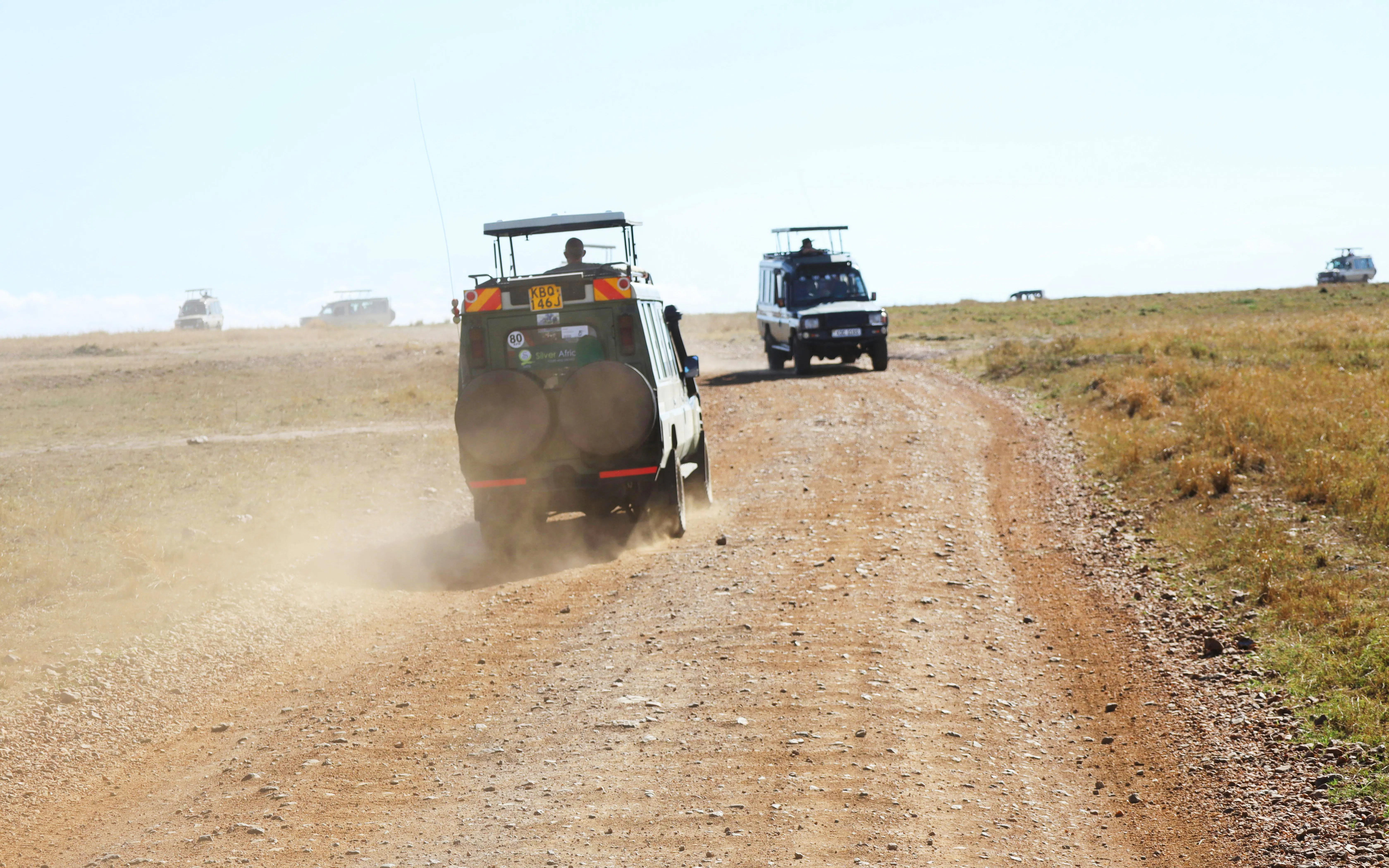 Safari jeeps driving on a dirt road in Masai Mara, Kenya.