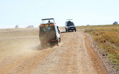 Safari jeeps driving on a dirt road in Masai Mara, Kenya.