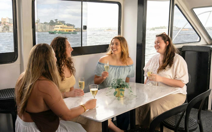Women enjoying drinks on Sydney Harbour sunset cruise with city view.