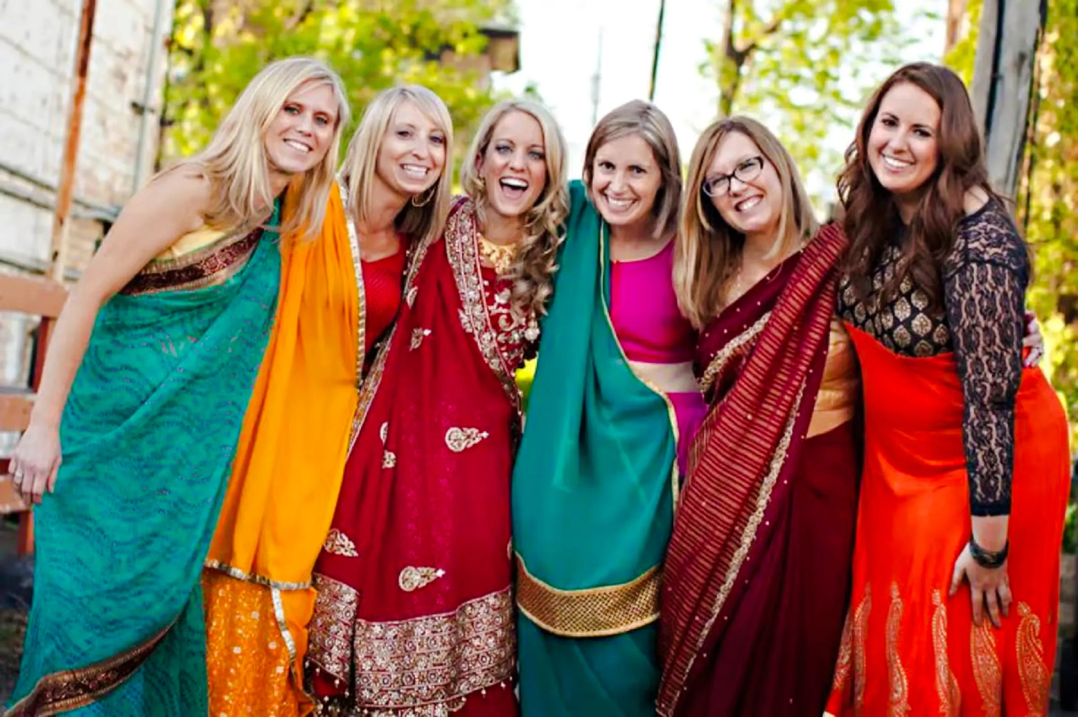 Women in colorful sarees smiling during a Delhi shopping tour with a female guide.