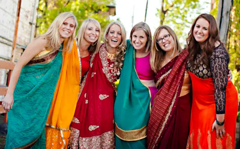 Women in colorful sarees smiling during a Delhi shopping tour with a female guide.