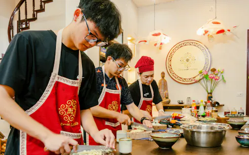 Participants preparing ingredients in a Hanoi vegan cooking class, wearing aprons and chopping vegetables.
