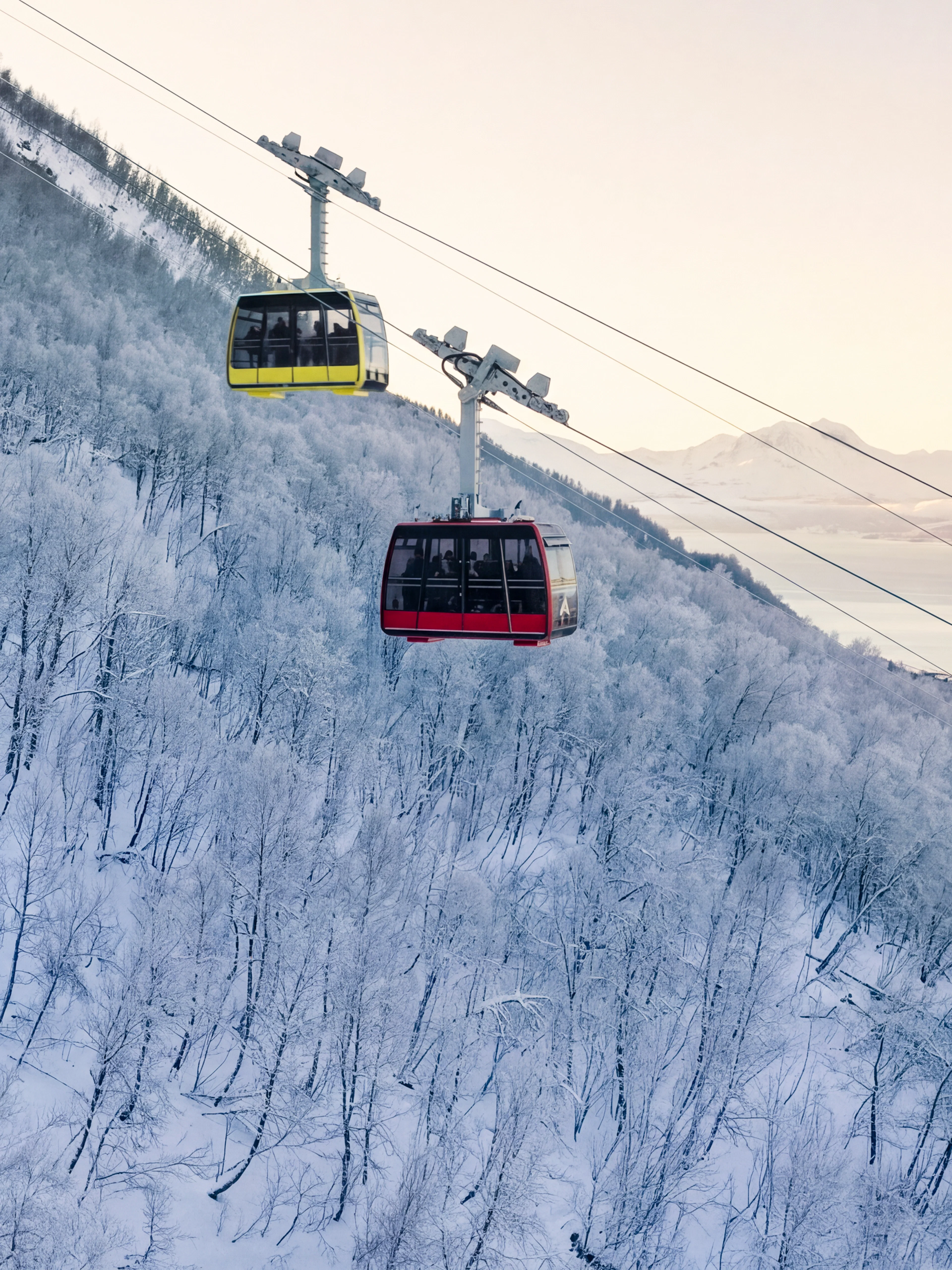 Cable cars ascending snowy Fjellheisen in Tromsø, Norway, with scenic mountain views.