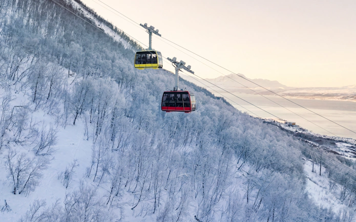 Cable cars ascending snowy Fjellheisen in Tromsø, Norway, with scenic mountain views.