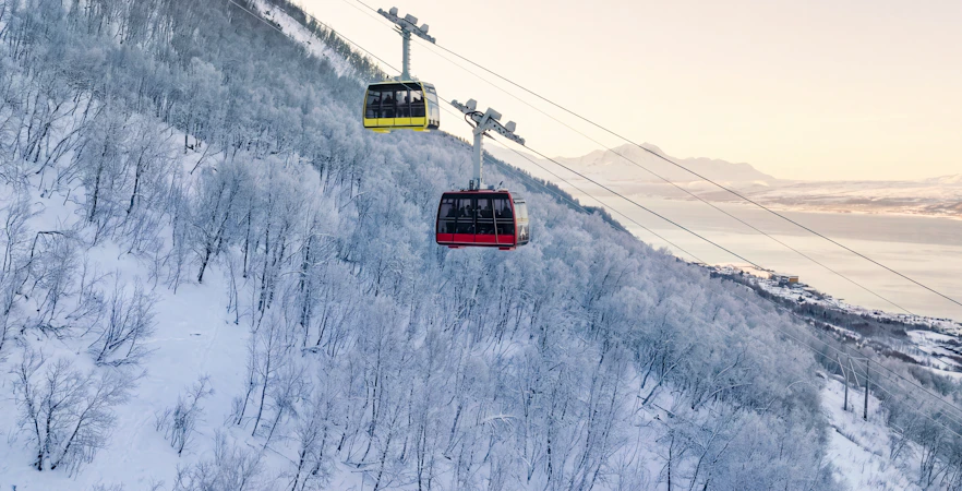 Cable cars ascending snowy Fjellheisen in Tromsø, Norway, with scenic mountain views.