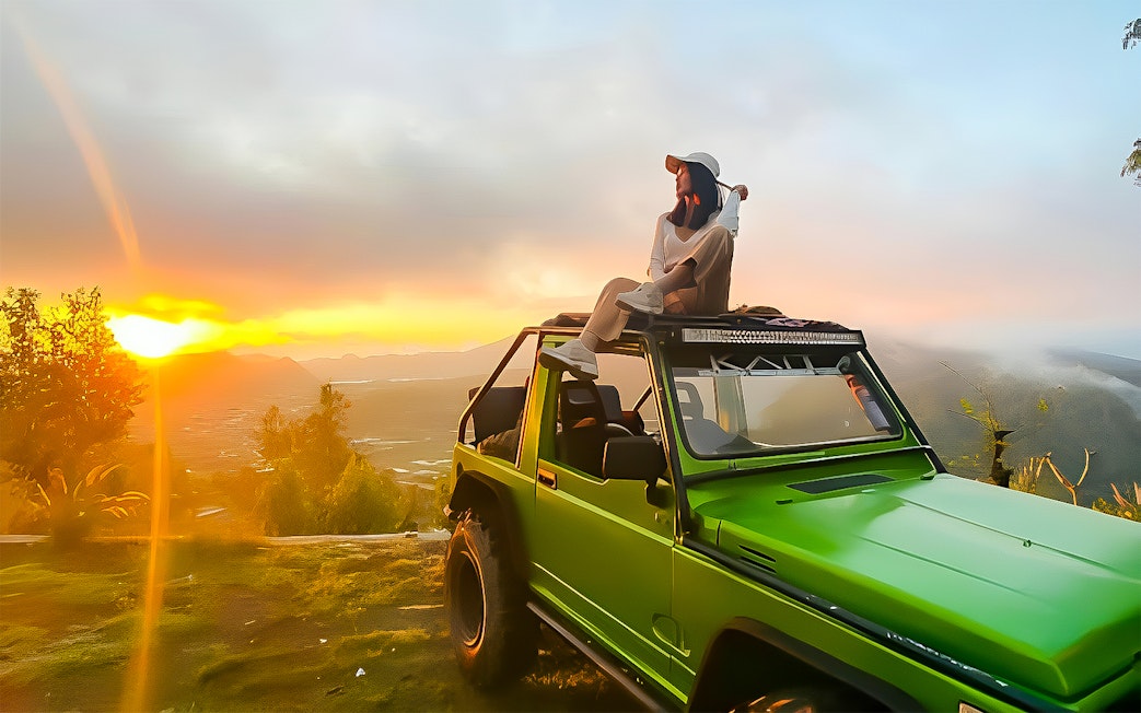 Person sitting on a green jeep at Mount Batur sunrise, Bali.
