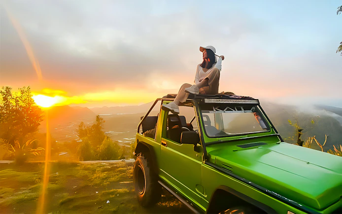 Person sitting on a green jeep at Mount Batur sunrise, Bali.