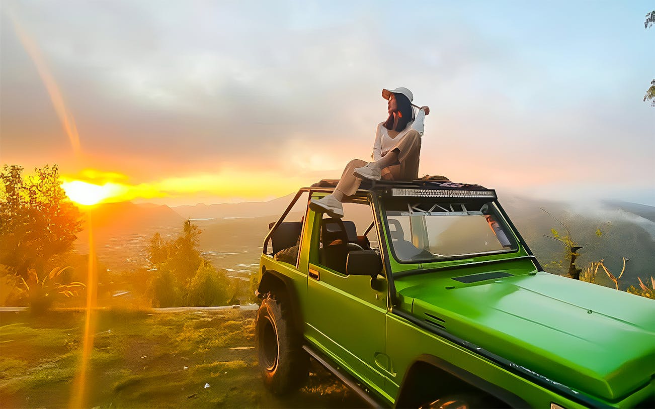 Person sitting on a green jeep at Mount Batur sunrise, Bali.