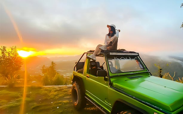 Person sitting on a green jeep at Mount Batur sunrise, Bali.