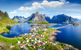 Reine village with rorbu houses, surrounded by mountains and water under a blue sky.