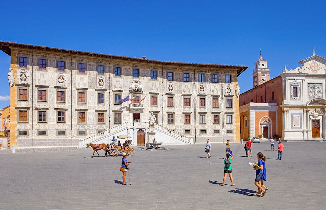 Scuola Normale Superiore at Piazza dei Cavalieri, Pisa, with tourists and a horse-drawn carriage.