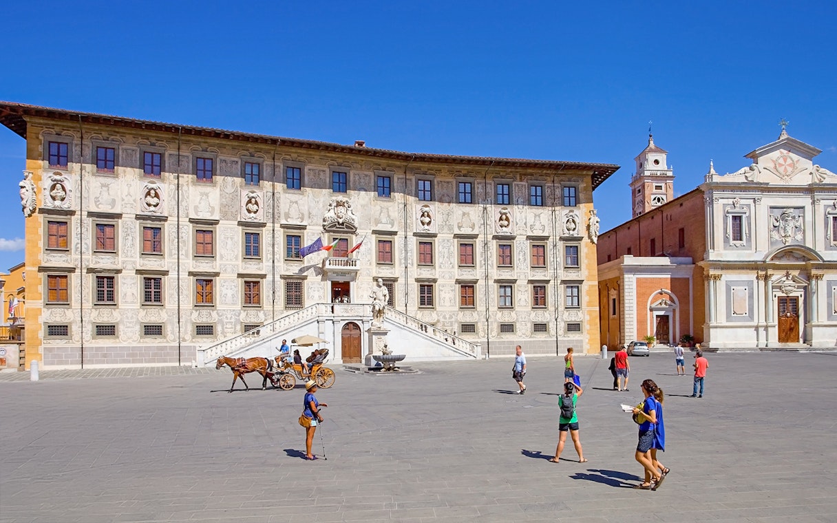 Scuola Normale Superiore at Piazza dei Cavalieri, Pisa, with tourists and a horse-drawn carriage.