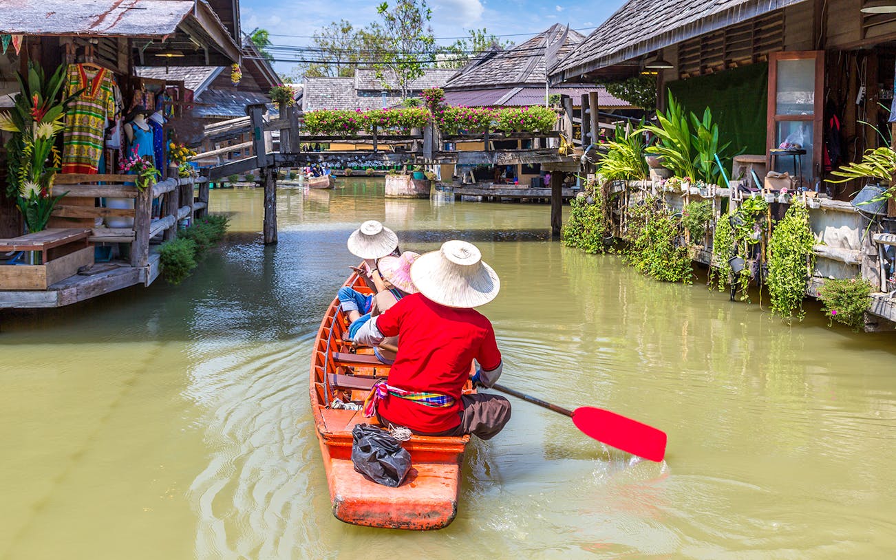 Boat navigating Pattaya floating market with people in traditional hats.