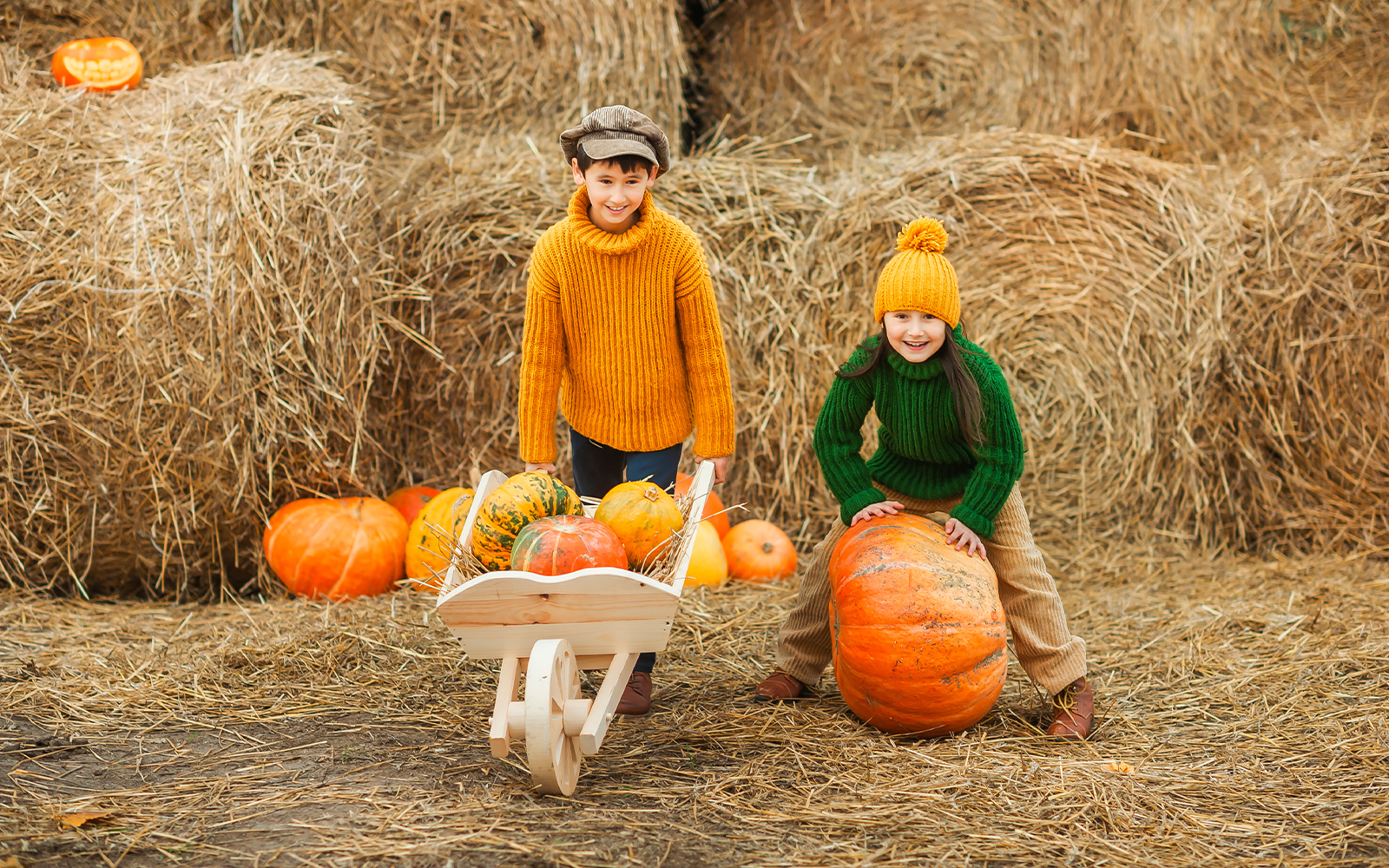 Children playing with pumpkins in an autumn setting with hay bales.