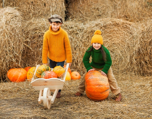 Children playing with pumpkins in an autumn setting with hay bales.