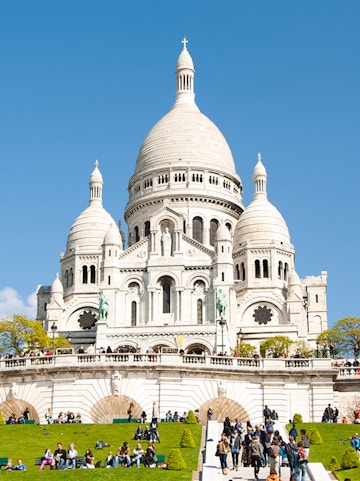 Sacre-Coeur Basilica in Montmartre, Paris, with visitors on the steps and lawn.