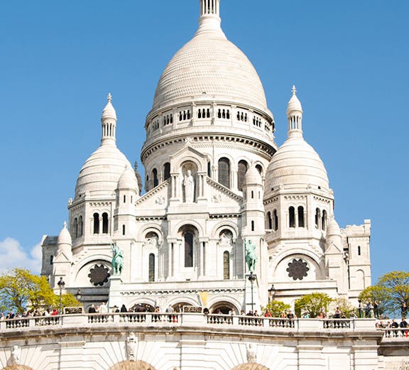 Sacre-Coeur Basilica in Montmartre, Paris, with visitors on the steps and lawn.