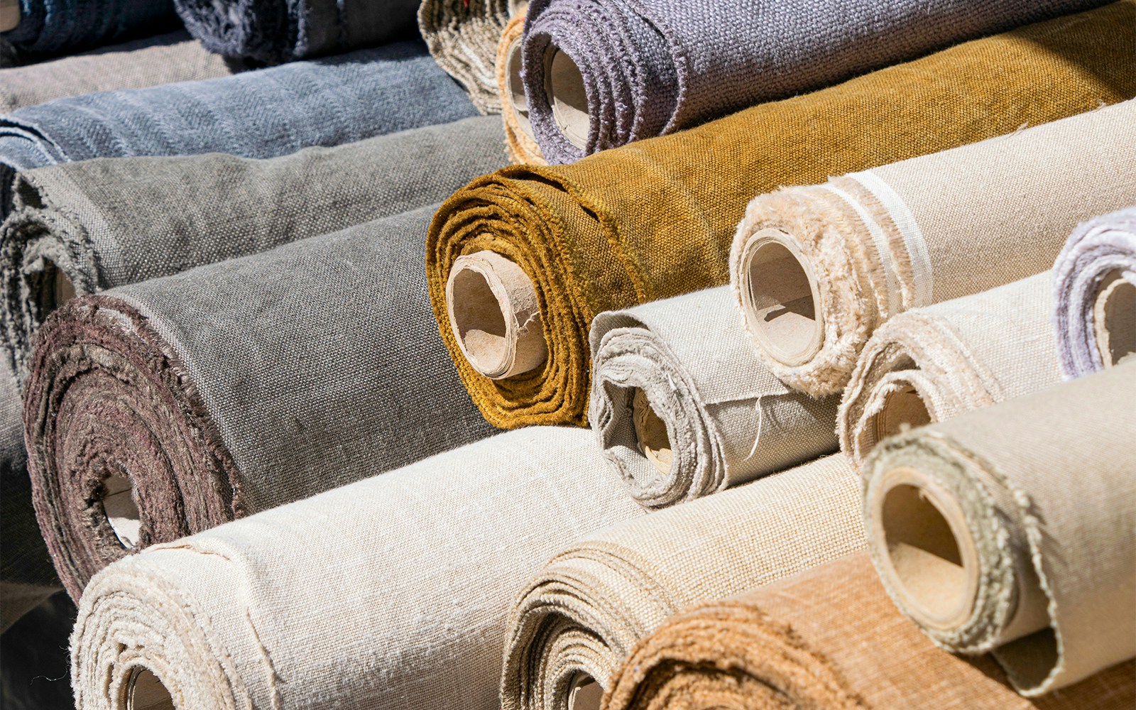 Rolls of linen canvas in various colors stacked together.