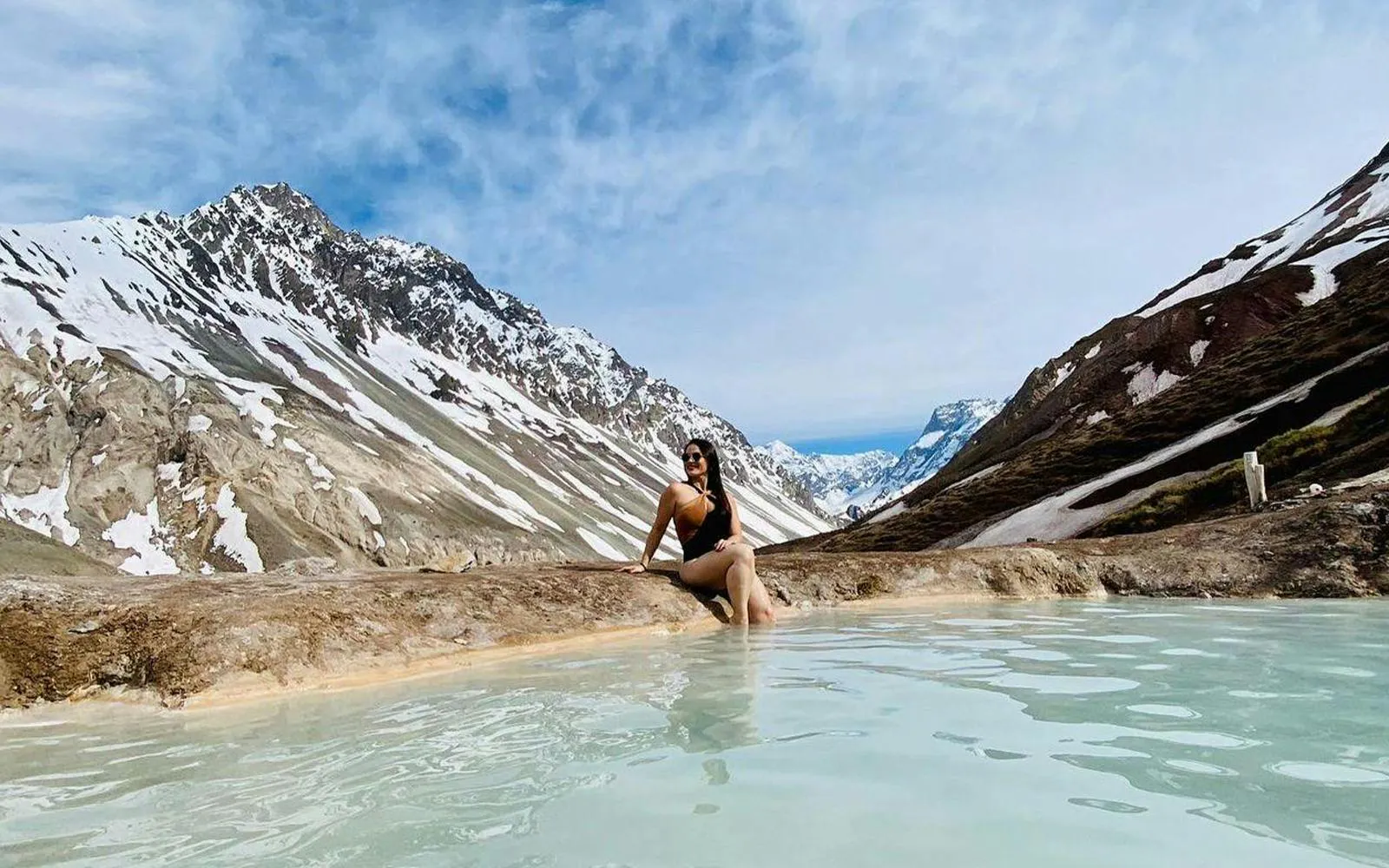 Person relaxing in hot spring with snowy Andes mountains in Cajon del Maipo, Santiago.