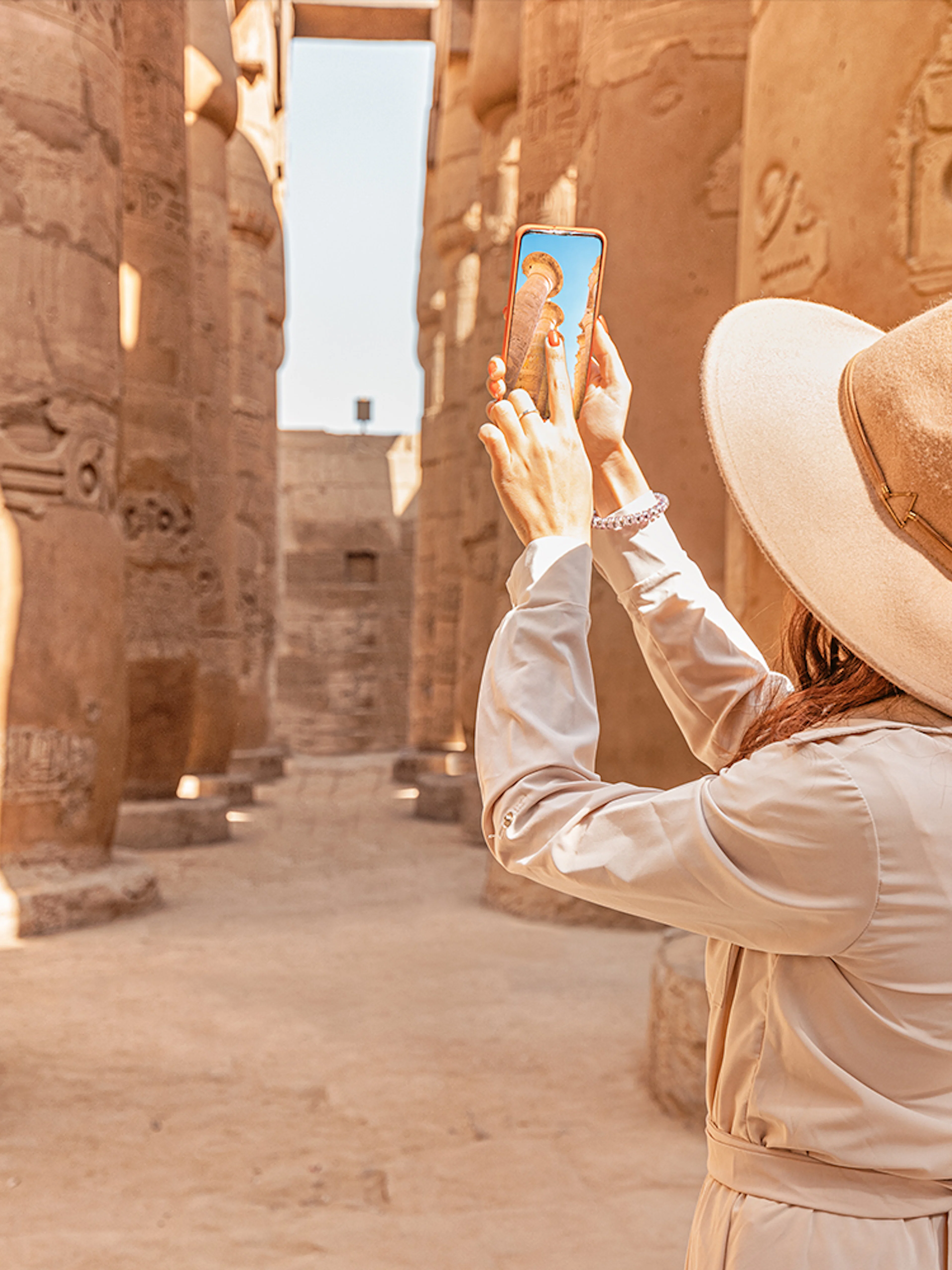Visitor using phone for audio tour at Karnak Temple, Egypt, surrounded by ancient columns.
