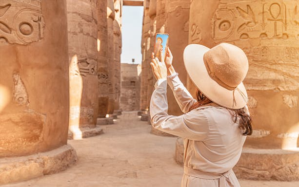 Visitor using phone for audio tour at Karnak Temple, Egypt, surrounded by ancient columns.