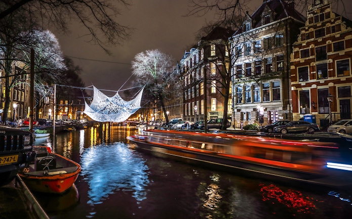Amsterdam canal with illuminated art installation during Light Festival cruise.