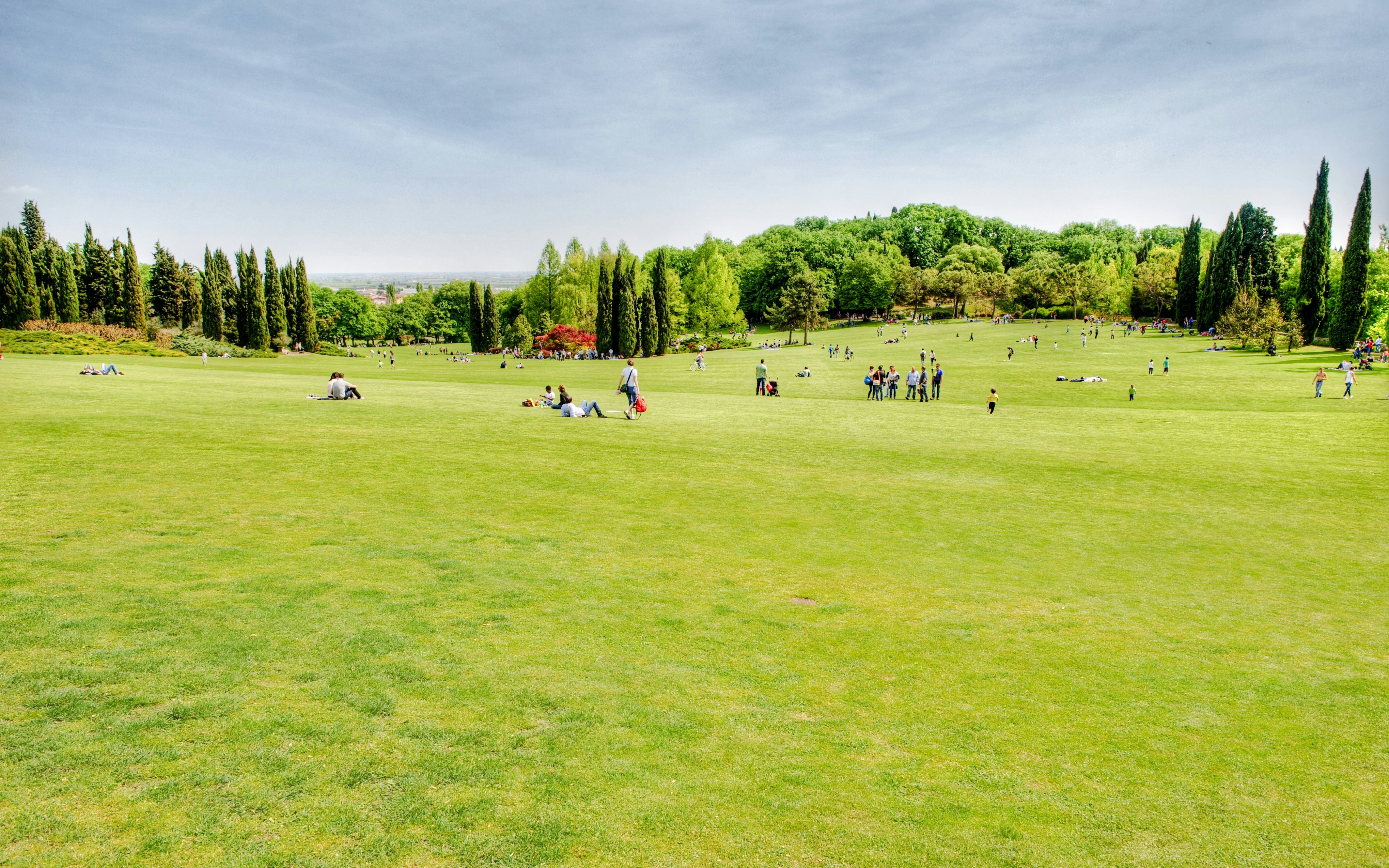 People relaxing and walking on the expansive green lawns of Sigurta Park, surrounded by trees.