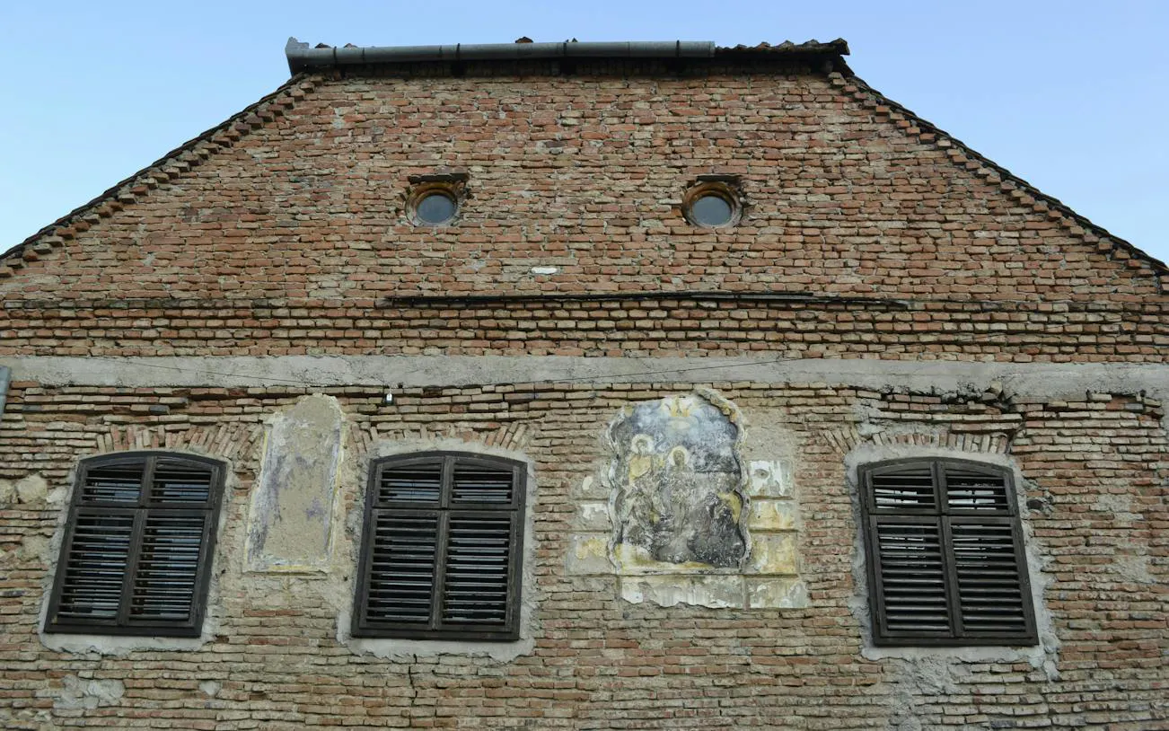 Historic brick building facade with mural in Schei, Brașov, part of self-guided city exploration game.