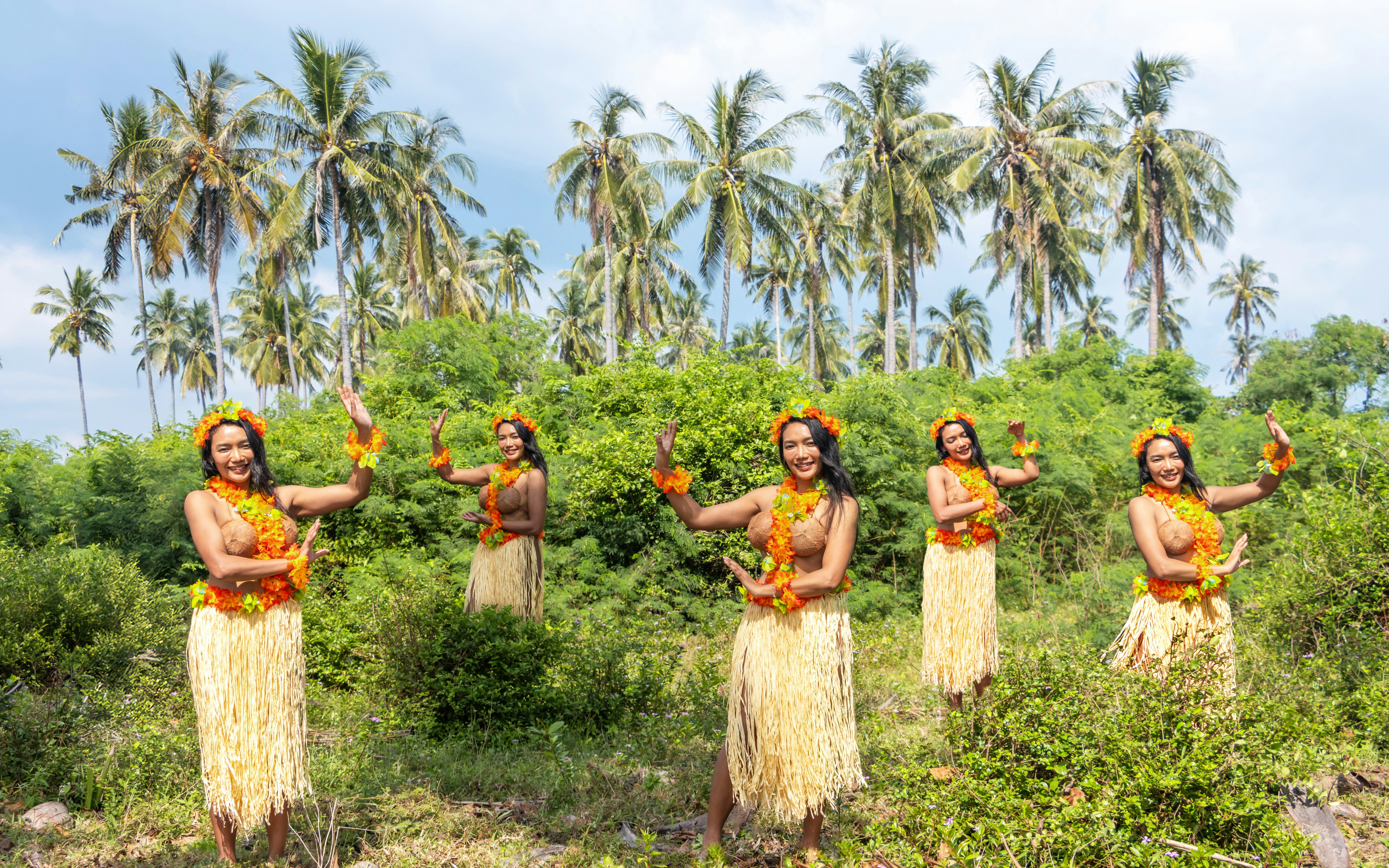 Hawaiian dancers performing hula in tropical setting with coconut palms.