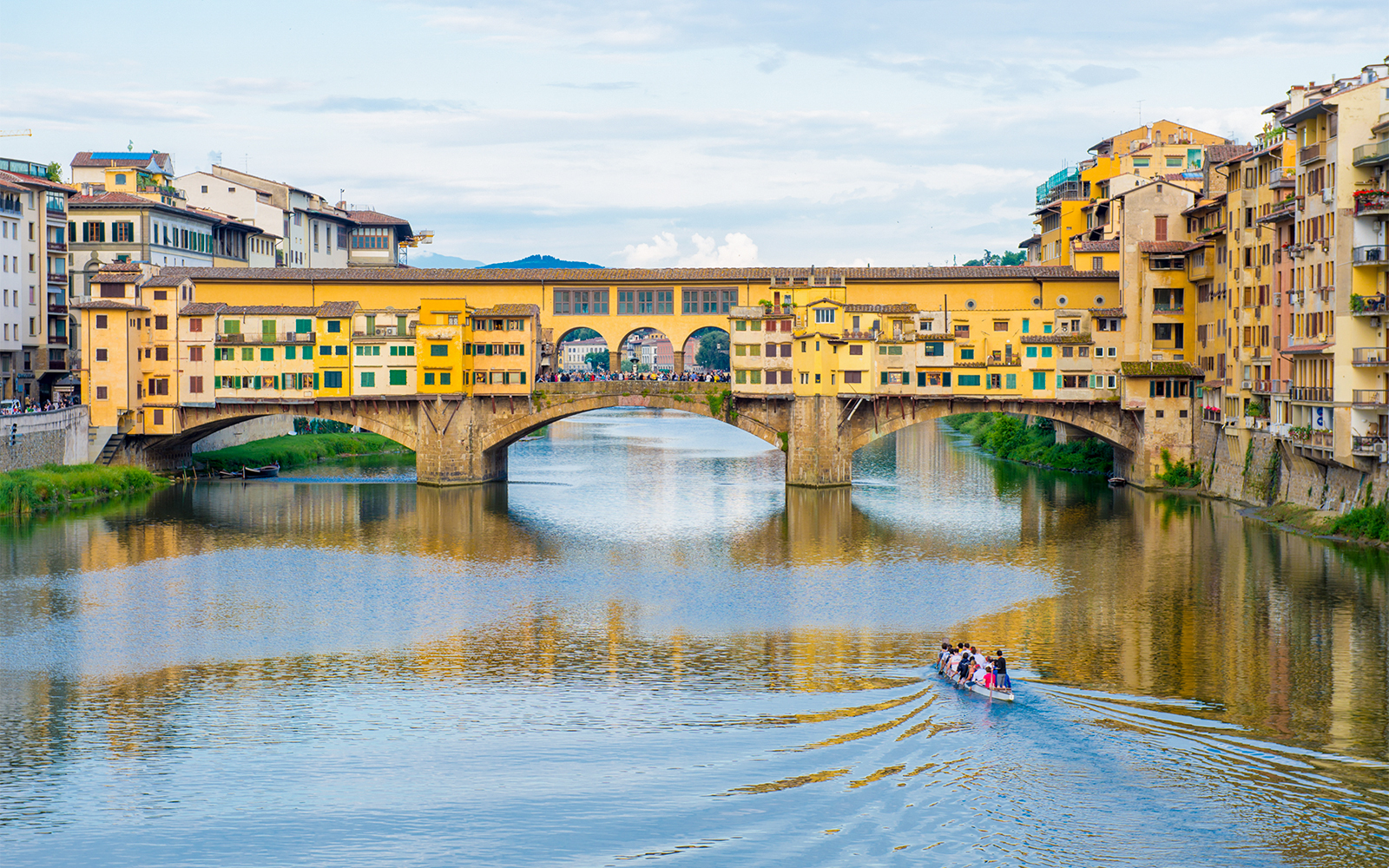 Ponte Vecchio bridge over Arno River in Florence with a boat tour passing underneath.