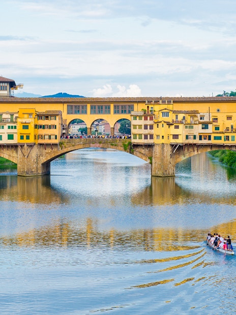 Ponte Vecchio bridge over Arno River in Florence with a boat tour passing underneath.