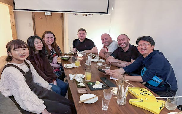 Group enjoying drinks at a table during Hiroshima local bar hopping night tour.