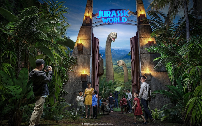 Visitors entering Jurassic World: The Experience with dinosaurs visible through the gate.