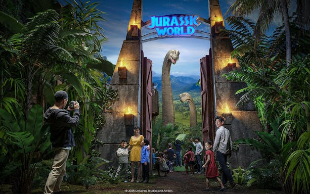 Visitors entering Jurassic World: The Experience with dinosaurs visible through the gate.
