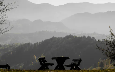 Wooden benches and table overlooking misty Carpathian mountains in Romanian village near Brasov.
