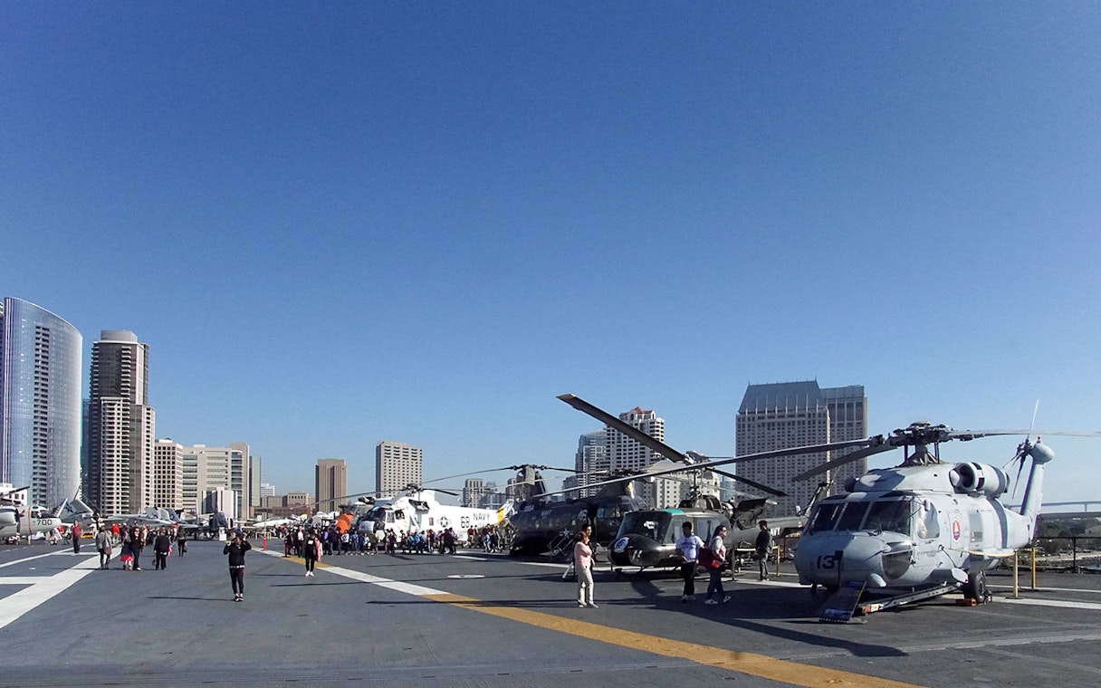 USS Midway Museum flight deck with helicopters and city skyline in San Diego.