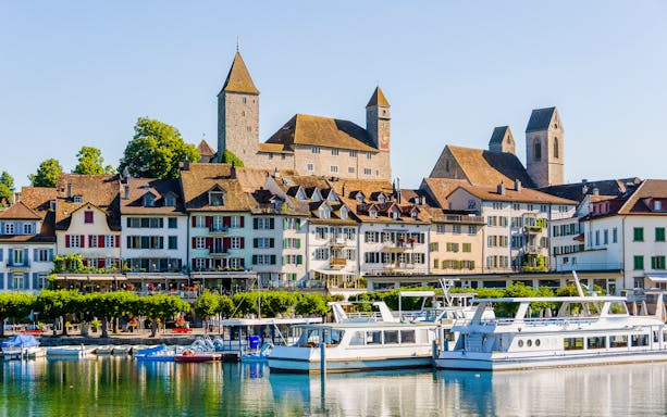 Rapperswil Castle overlooking Lake Zurich with boats docked in the foreground.
