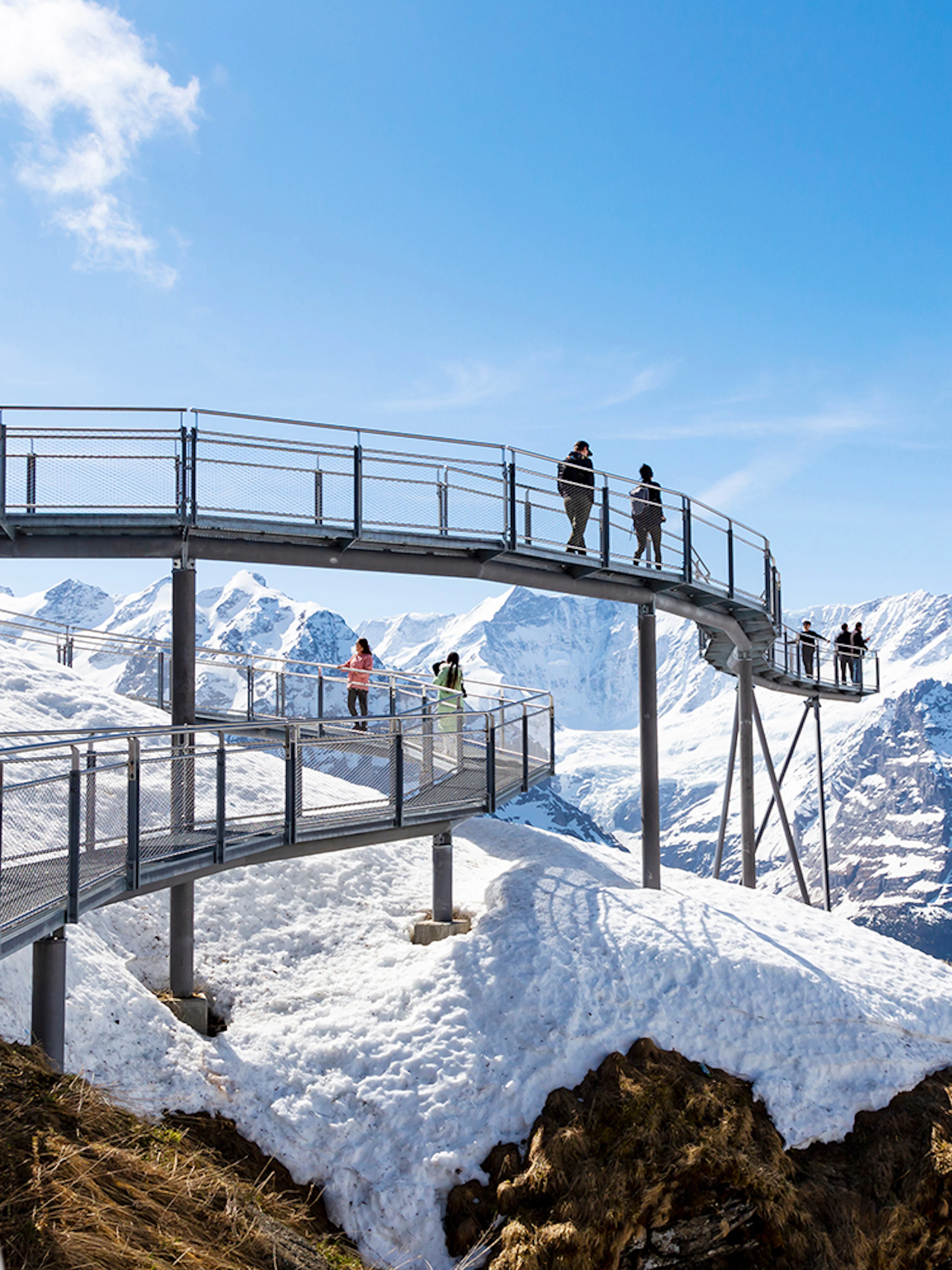 Visitors on a metal walkway with snowy mountain views in Grindelwald, Switzerland.