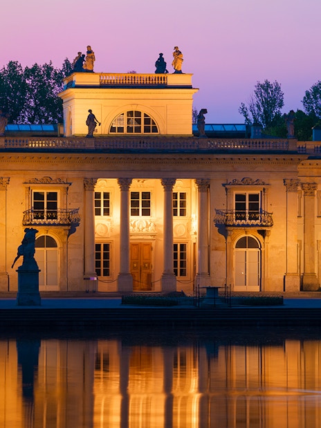 Lazienki Palace in Warsaw at sunset reflecting on the water.