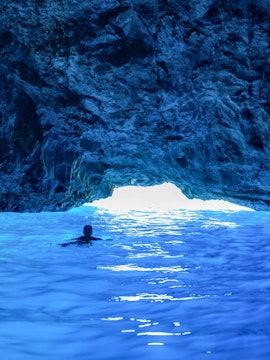 Swimmer exploring Dubrovnik Blue Cave with sunlight illuminating the water.