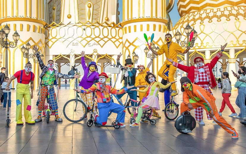 Clowns performing at Global Village Dubai entrance with colorful costumes and unicycles.