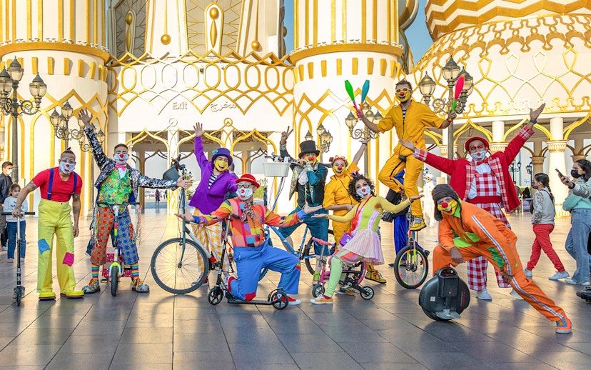 Clowns performing at Global Village Dubai entrance with colorful costumes and unicycles.