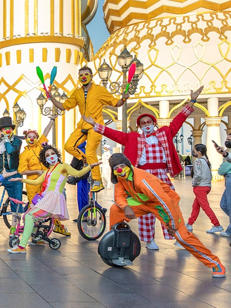 Clowns performing at Global Village Dubai entrance with colorful costumes and unicycles.