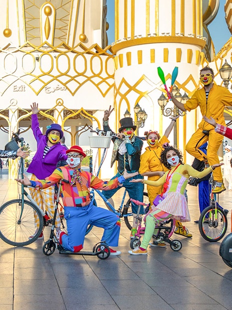 Clowns performing at Global Village Dubai entrance with colorful costumes and unicycles.
