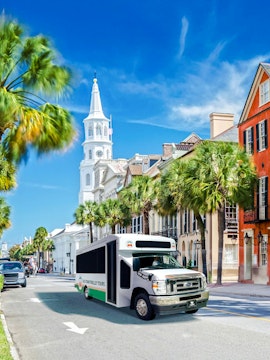 Charleston trolley passing historic buildings and palm trees on a sunny day.