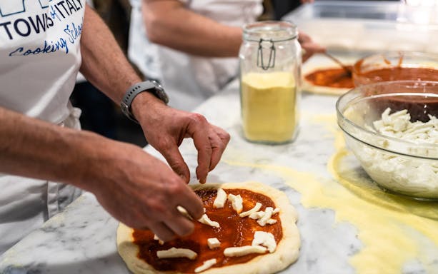 Hands preparing pizza dough with tomato sauce and cheese during a cooking class.
