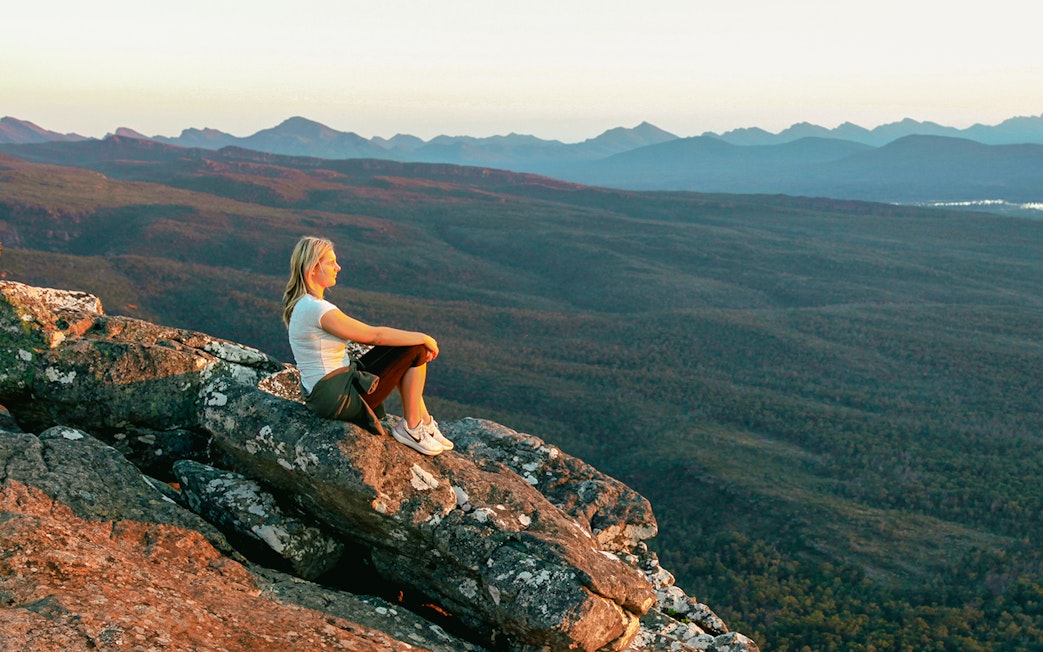 Person sitting on rock overlooking Grampians National Park during 1-day guided tour from Melbourne.