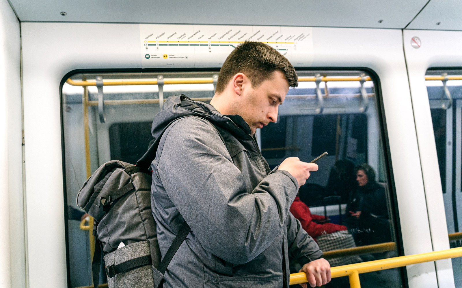 Man using phone on Copenhagen metro with city map above.