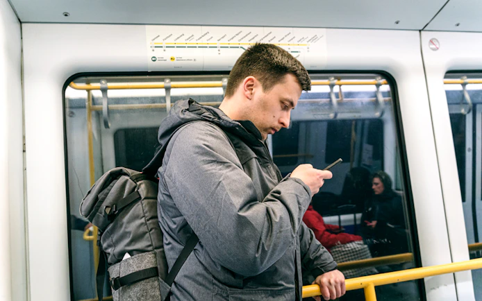 Man using phone on Copenhagen metro with city map above.